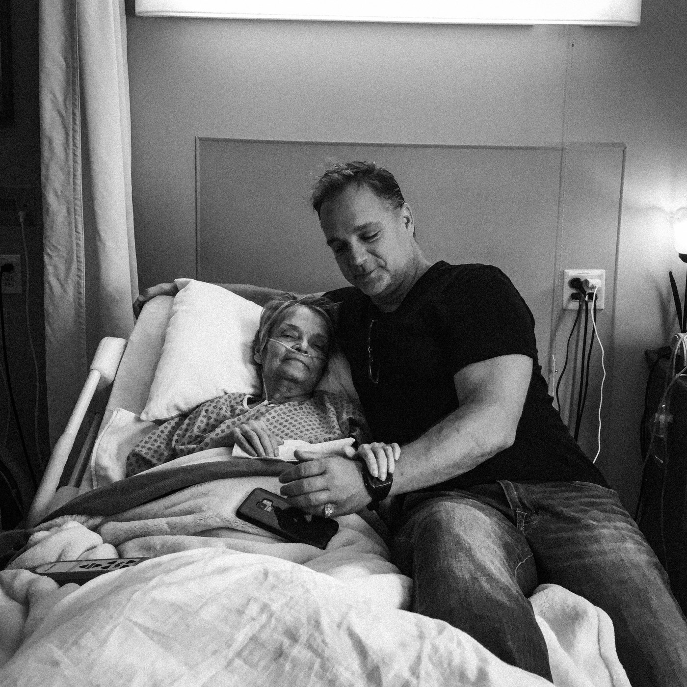 The author sitting on a hospital bed, holding his mother's hand